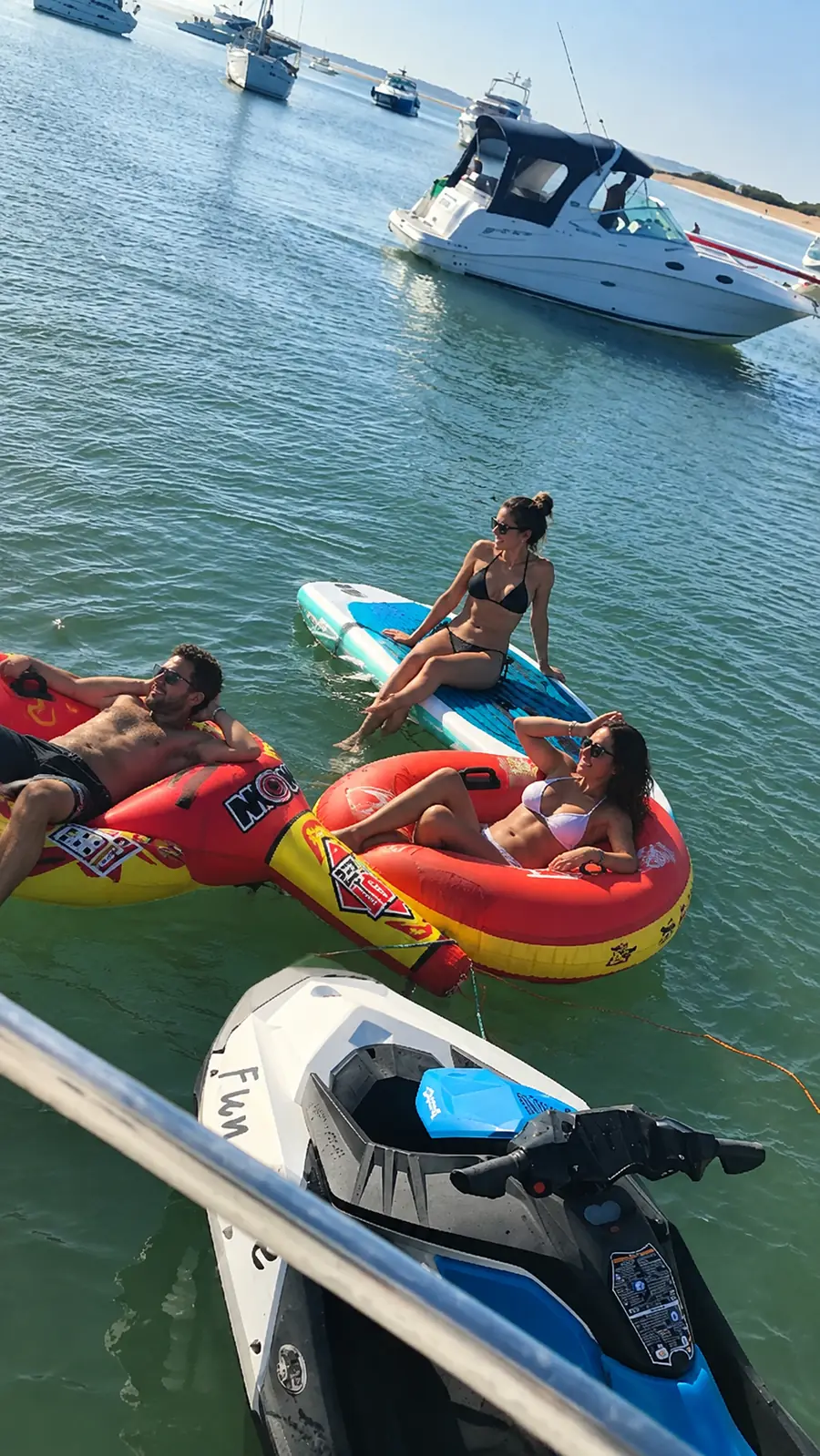 Amigos disfrutando sobre una dona y un paddle junto a una moto de agua durante un paseo en yate en Punta del Este